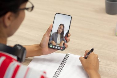 Gülümseyen Afro-Amerikan iş kadını Asyalı bir meslektaşın günlüğe yazdığı video çağrısında. Değiştirilmemiş iş, kablosuz teknoloji, toplantı, çalışma, takım çalışması ve ofis konsepti.