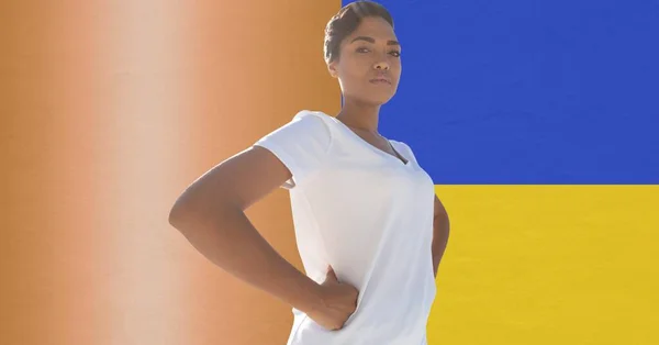 Portrait of african american woman with hands on hips against ukraine flag design background. ukraine crisis, invasion and international relations concept