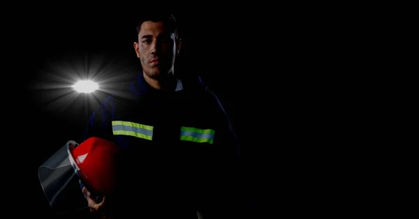 Caucasian firefighter holding a helmet against spot of light and copy space on black background. safety concept