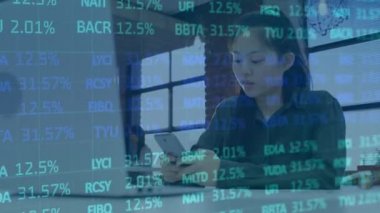Ofiste akıllı telefon kullanan Asyalı iş kadınına karşı borsa veri işleme. küresel finans ve iş teknolojisi kavramı