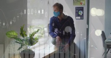 Pencerede oturan beyaz maskeli bir adam için finansal grafiklerin animasyonu. İş, iletişim, teknoloji ve covdi 19 salgın konsepti dijital olarak oluşturulmuş video.