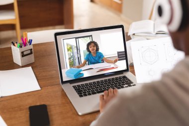 Afrika kökenli Amerikalı öğrenci evde internetten okurken arkadaşlarıyla görüntülü konuşma yapıyor. Dizüstü bilgisayar, ekran, değiştirilmemiş, çocukluk, kablosuz teknoloji, eğitim, internet, e-öğrenim kavramı.