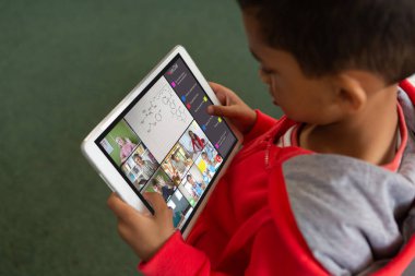 Evde dijital tablet üzerine çevrimiçi derste video üzerinden öğrenen melez bir çocuğun yüksek açılı görüntüsü. İnternet, ekran, değiştirilmemiş, çocukluk, kablosuz teknoloji, eğitim, öğrenci ve e-öğrenim.