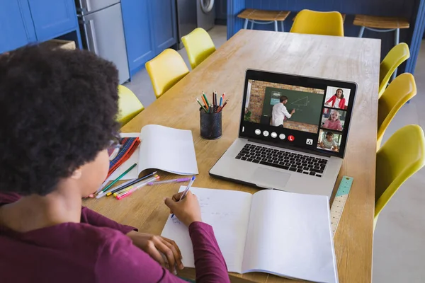 African american girl writing in notebook while teacher giving notes over video call on laptop. Online, unaltered, childhood, wireless technology, education, screen, student and e-learning concept.