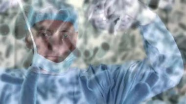 Animation of covid 19 cells over caucasian male surgeon wearing face mask in operating theatre. global covid 19 pandemic, medicine and healthcare services concept digitally generated video.