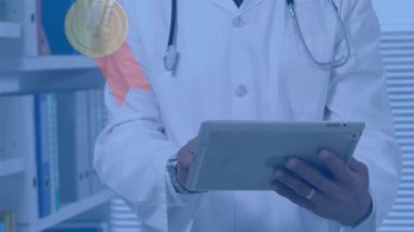 Animation of medals over biracial male doctor with tablet. national heart day and celebration concept digitally generated video.