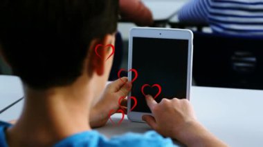 Sınıfta dijital tablet kullanan beyaz bir çocuğun dikiz aynasında birden fazla kırmızı kalp simgesi var. Okul ve eğitim kavramı