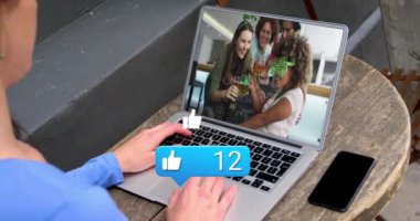 Like icon with increasing numbers over caucasian woman having a videocall on laptop at a cafe. Social media networking and business technology concept