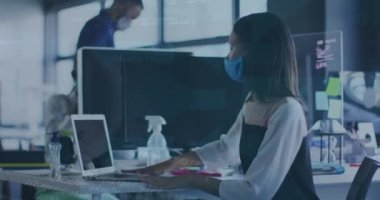 Animation of data processing over biracial businesswoman in face mask in office. Global covid 19 pandemic, business, finance, data processing and networking concept digitally generated video.