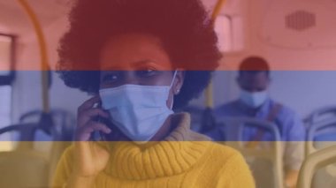 Otobüste akıllı telefon kullanarak Kolombiya bayrağını yüz maskesi takan Afro-Amerikan kadının üzerine dikmek. Küresel seyahat, ulaşım ve vatanseverlik kavramı dijital olarak oluşturuldu.