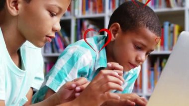 Multiple red heart icons floating over two diverse boys using laptop at school. School and education concept