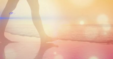 Animation of light spots over woman walking at beach. Global business and digital interface concept digitally generated video.