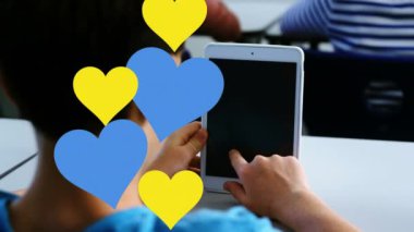 Okulda dijital tablet kullanan beyaz bir çocuğun dikiz aynasında birden fazla mavi ve kırmızı kalp simgesi var. Okul ve eğitim kavramı