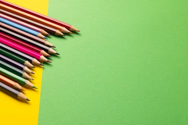 Sarı ve yeşil yüzeydeki renkli boya kalemlerinin kompozisyonu. Okul ekipmanları, çizim araçları, şablon ve yaratıcılık kavramı.