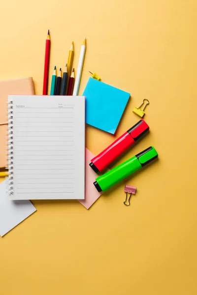 Vertical composition of notebook with copy space and school equipment on yellow surface. School equipment, tools and creativity concept.