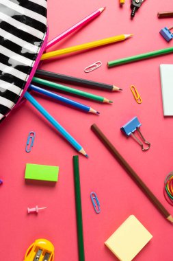 Çizgili çantadaki boya kalemlerinin dikey bileşimi. Pembe yüzeydeki klipsler ve bileyiciler. Okul ekipmanları, araçlar ve yaratıcılık kavramı.