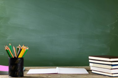 Kara tahtanın üzerindeki tahta masada kitap, defter ve elma resmi. Eğitim, öğrenme ve yaratıcılık