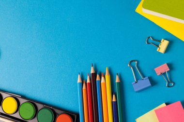 Suluboya, pastel boya ve klipslerin mavi yüzeyde fotokopi alanı ile bileşimi. Okul ekipmanları, araçlar ve yaratıcılık kavramı.