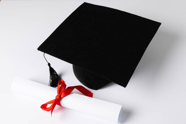 Image of graduation hat and diploma on white surface. School, learning, education and graduation concept.
