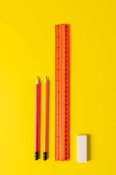 Vertical composition of rulers, pencils and eraser on yellow surface. School equipment, tools, education and creativity concept.
