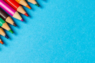 Mavi yüzeyde fotokopi alanı olan renkli boya kalemlerinin bileşimi. Okul ekipmanları, çizim araçları, şablon ve yaratıcılık kavramı.