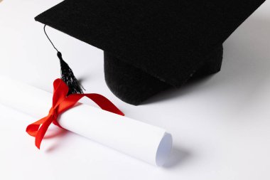 Image of graduation hat and diploma on white surface. School, learning, education and graduation concept.