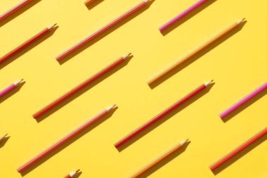 Imagine of crayons of different shades of pink on yellow background. Education, learning and creativity.