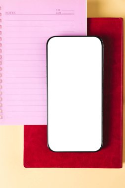 Sarı yüzey üzerinde kopya alanı ve not defterleri olan akıllı telefonun dikey bileşimi. Okul ekipmanları, araçlar, teknoloji ve yaratıcılık kavramı ile öğrenme.