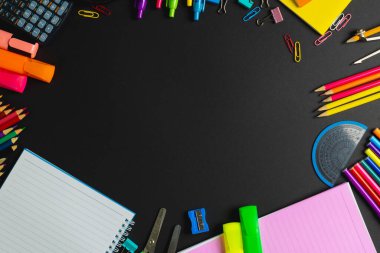 Composition of frame made of colorful school tools on black surface with copy space. School equipment, tools and creativity concept.