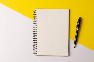 Sarı ve beyaz yüzey üzerinde kopya alanı ve kalem olan bir defter resmi. İş, ofiste çalışmak, ekipman ve araç gereç kavramı.