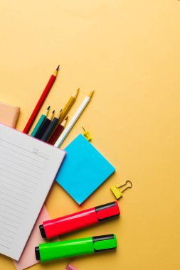 Not defterinin dikey kompozisyonu kopya alanı ve sarı yüzey üzerindeki okul ekipmanı. Okul ekipmanları, araçlar ve yaratıcılık kavramı.