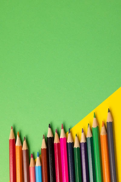 Vertical composition of colorful crayons on yellow and green surface with copy space. School equipment, drawing tools, pattern and creativity concept.