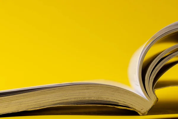 Image of open book on yellow surface with copy space. School equipment, tools, learning and education concept.