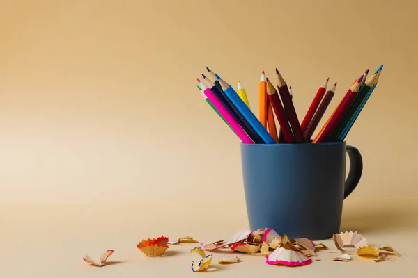 Composition of colorful crayons in blue mug on yellow surface with copy space. School equipment, drawing tools, pattern and creativity concept.