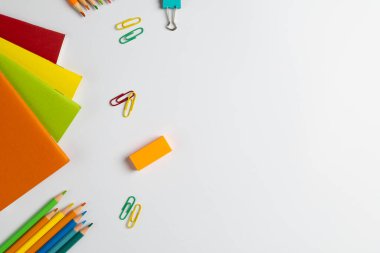 Beyaz yüzeyde fotokopi alanı olan not defterleri, klipler ve pastel boyaların bileşimi. Okul ekipmanları, araçlar ve yaratıcılık kavramı.