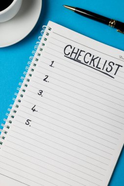 Vertical image of notebook with checklist and copy space, coffee and pen on blue surface. Business, working in office, equipment and tools concept.