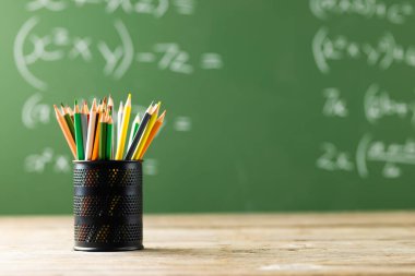 Siyah tahtadaki matematiksel formüllerin üzerinde boya kalemleri olan fincan resmi. Eğitim, öğrenme ve yaratıcılık