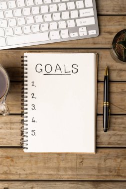 Amaçlı bir defterin dikey görüntüsü ve ahşap yüzeyde kahve ve dizüstü bilgisayarla kopyalama alanı. İş, görevler, ofis ekipmanları ve not alma kavramı.