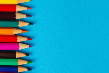 Mavi yüzeyde fotokopi alanı olan renkli boya kalemlerinin bileşimi. Okul ekipmanları, çizim araçları, şablon ve yaratıcılık kavramı.