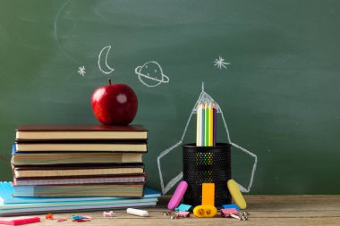 Image of school supplies, apple and notebook over drawings on black board. Education, learning and creativity