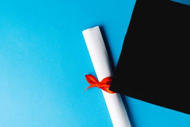 Mavi yüzeyde mezuniyet şapkası ve diploması. Okul, öğrenim, eğitim ve mezuniyet kavramı.