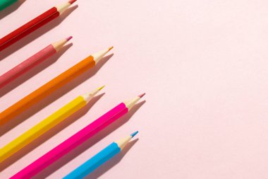 Composition of colorful crayons on pale pink surface with copy space. School equipment, drawing tools and creativity concept.