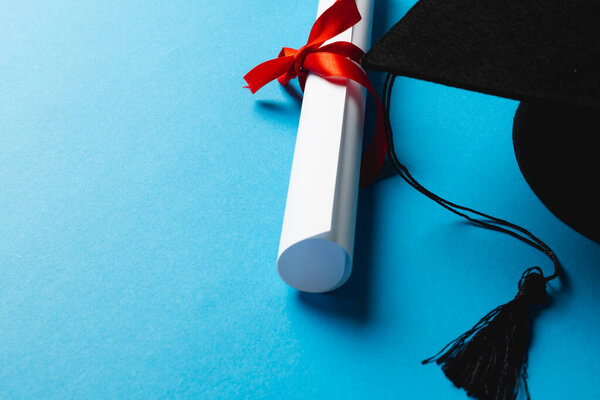 Image of graduation hat and diploma on blue surface. School, learning, education and graduation concept.