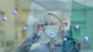 Animation of virus cells and flag of ivory coast over caucasian woman with face mask. Global pandemic, patriotism and digital interface concept digitally generated video.