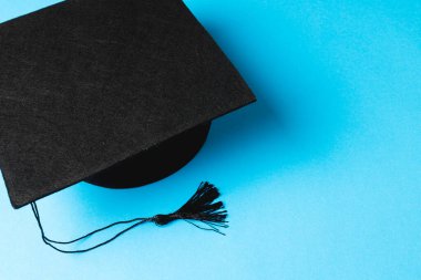 Image of black graduation hat lying on blue surface. School, learning, education and graduation concept.