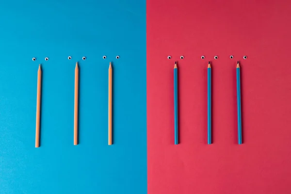 Composition of pencils with eyes on blue and pink surface. School equipment, tools, learning and creativity concept.