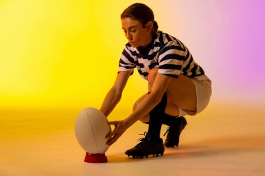 Beyaz kadın rugby oyuncusu, neon pembe ışıkta rugby topuyla çömeliyor. Spor, hareket, eğitim ve aktif yaşam tarzı kavramı.
