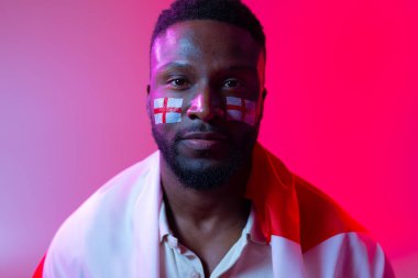 Image of serious african american male soccer fan with flag of england in neon pink lighting. Sport, fans, cheering and emotions concept.