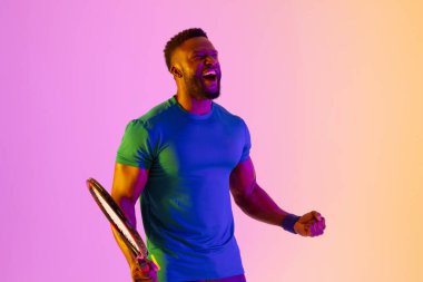 Image of successful african american male tennis player in violet and yellow lighting. Sport, movement, fitness and active lifestyle concept.
