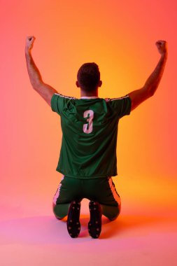 Caucasian male soccer player raising hands over neon pink lighting. Sport, movement, training and active lifestyle concept.